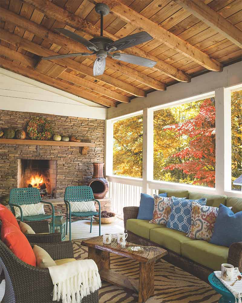 A screened-in porch with a stone fireplace and overhead fan. 