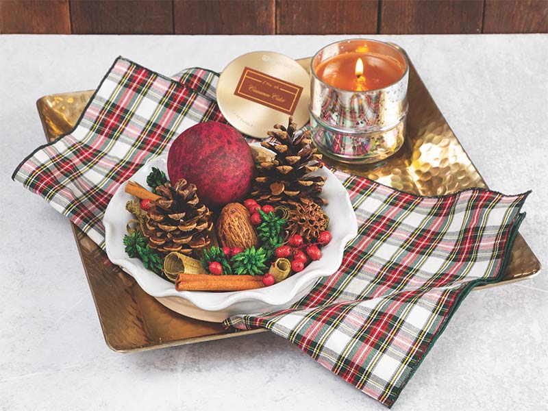 A gold tray with a plaid napkin, a white ruffled pie dish filled with potpourri, and a mercury glass candle.