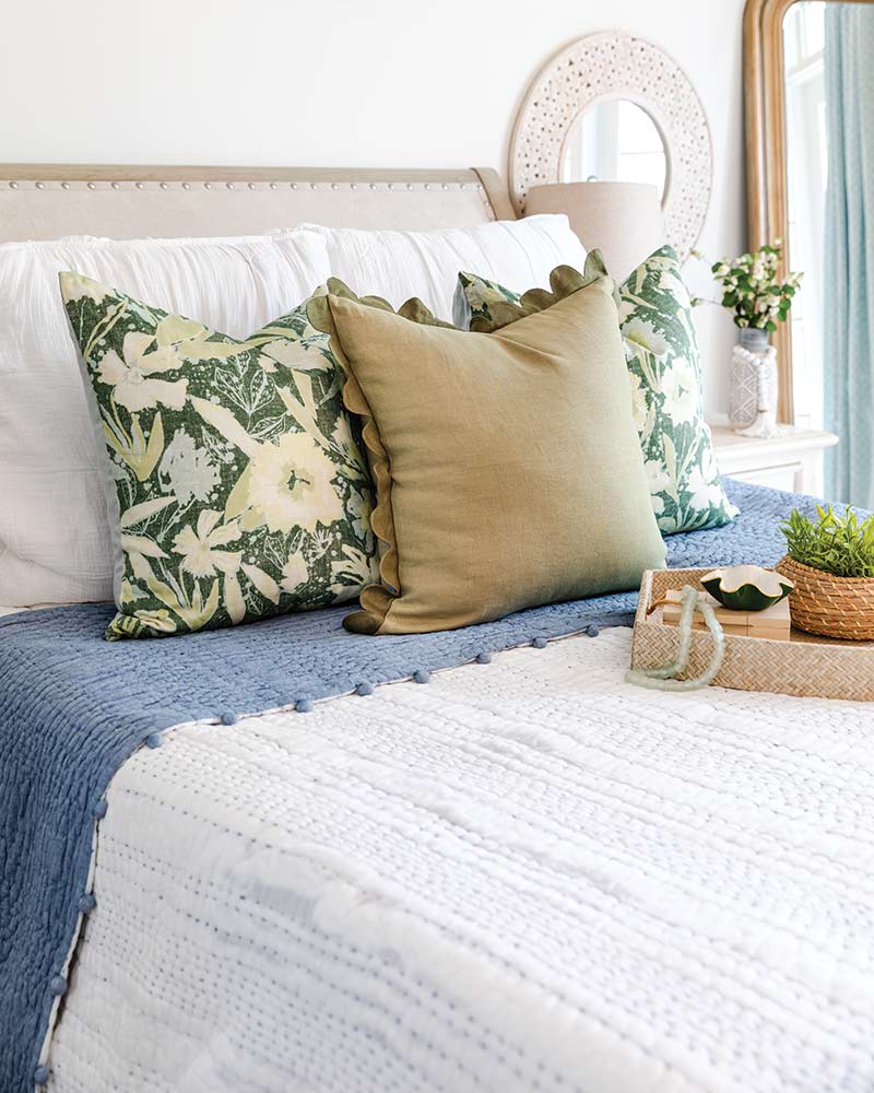 A bed with green floral accent pillows and a sage accent pillow.