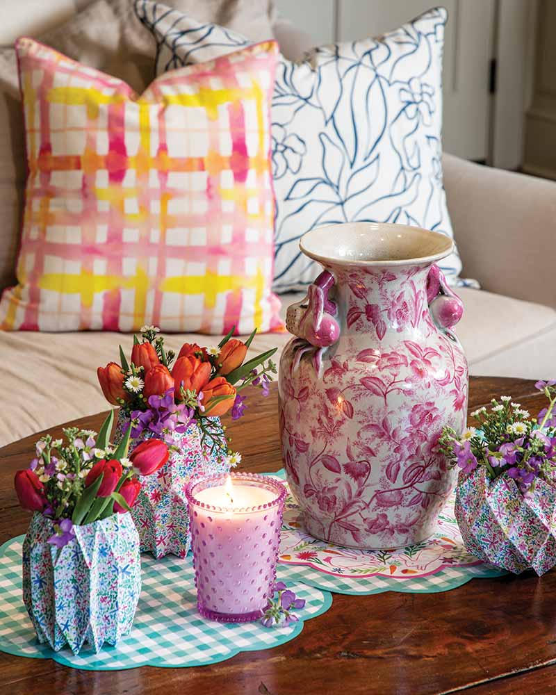A coffee table with pink chinoiserie, a candle, and colorful vase covers.