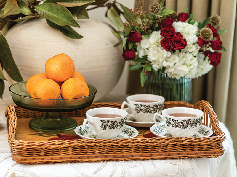 A tray of teacups and a bowl of oranges. 