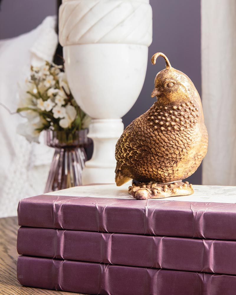 A stack of purple books and gold bird figurine.