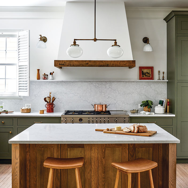A kitchen with an oak island, surround cabinets painted sage, and white countertops. 