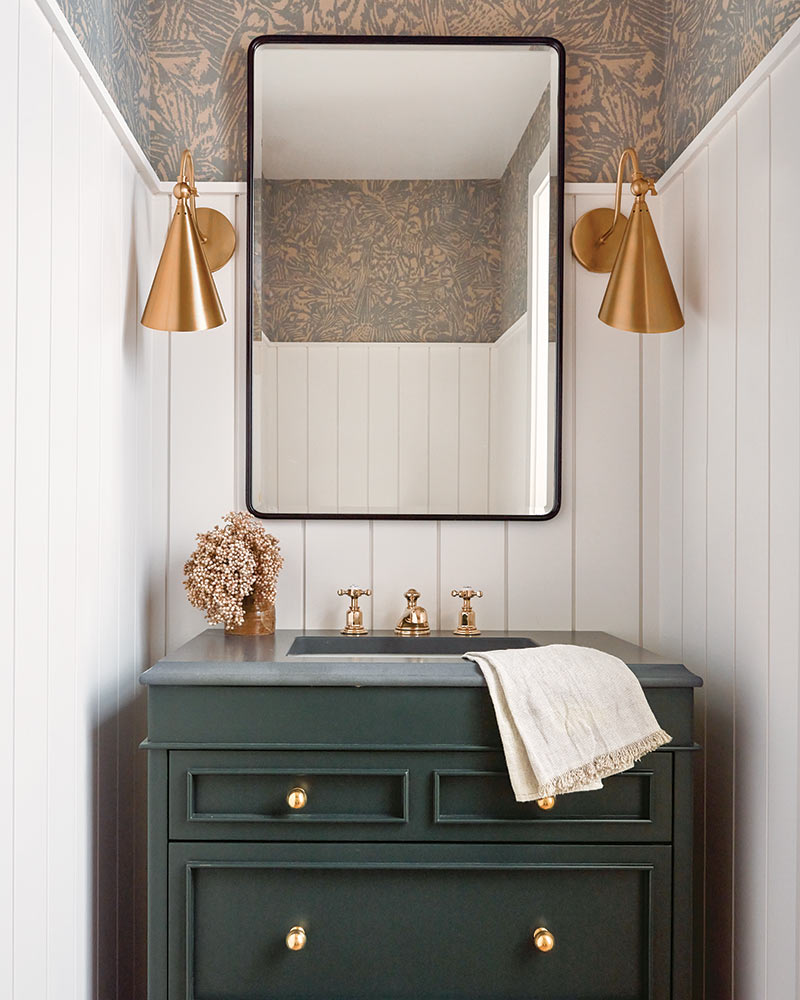 A powder bathroom with a green vanity and brass fixtures.