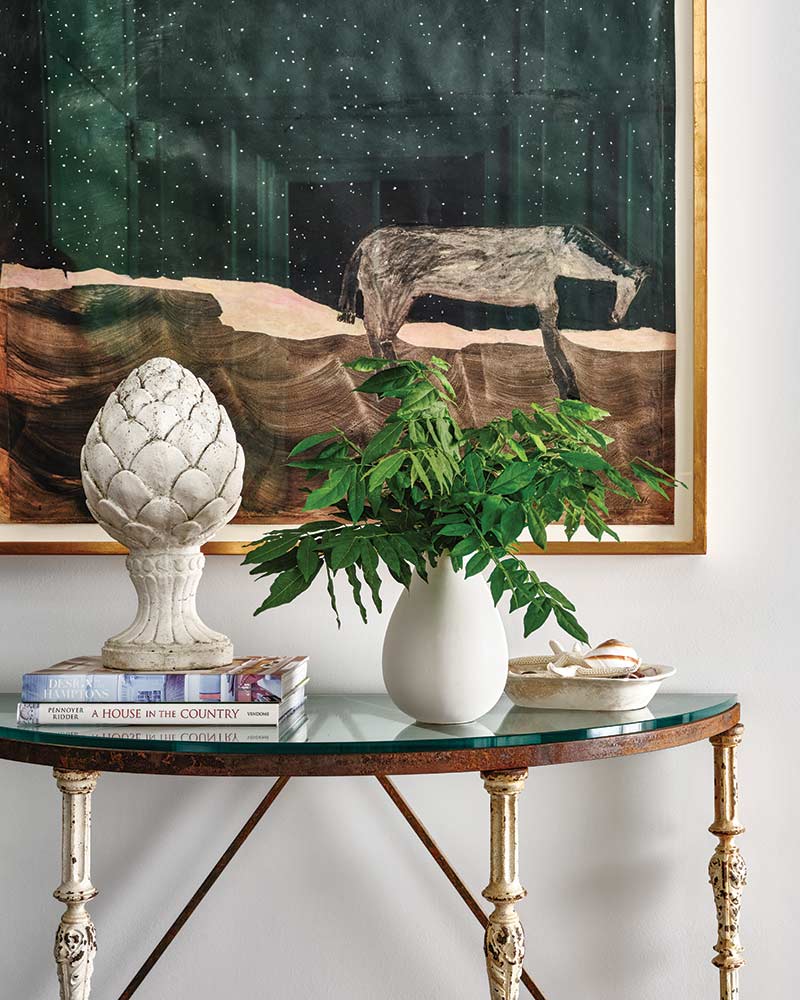 A console table with a sculpture and plant in front of a large piece of artwork.