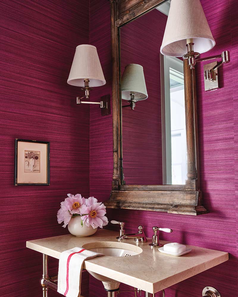 A powder bath with magenta grass cloth wallpaper.