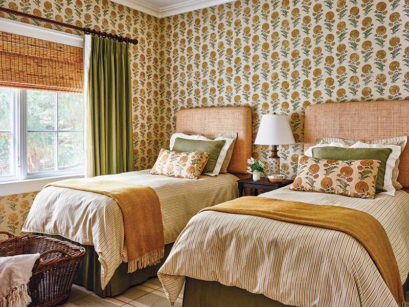 A bedroom with two beds and golden yellow botanical block print wallpaper. 