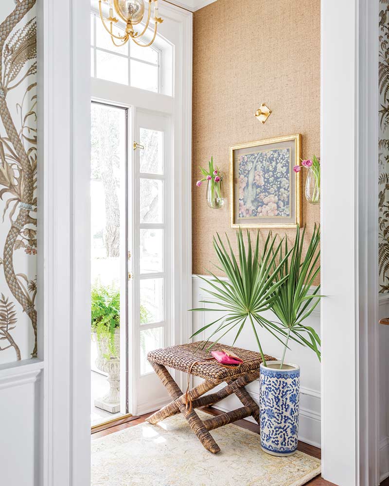 An entry with beige grasscloth wallpaper and an upholstered stool. 