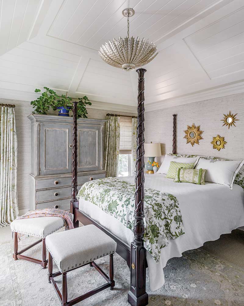 A bedroom with white and green bedding, a four poster bed, and sunburst mirrors.