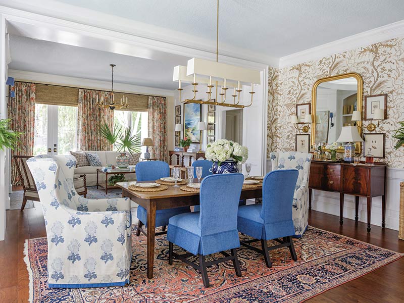 A dining room with an antique rug, blue velvet upholstered side chairs, and host chairs with block print slip covers.