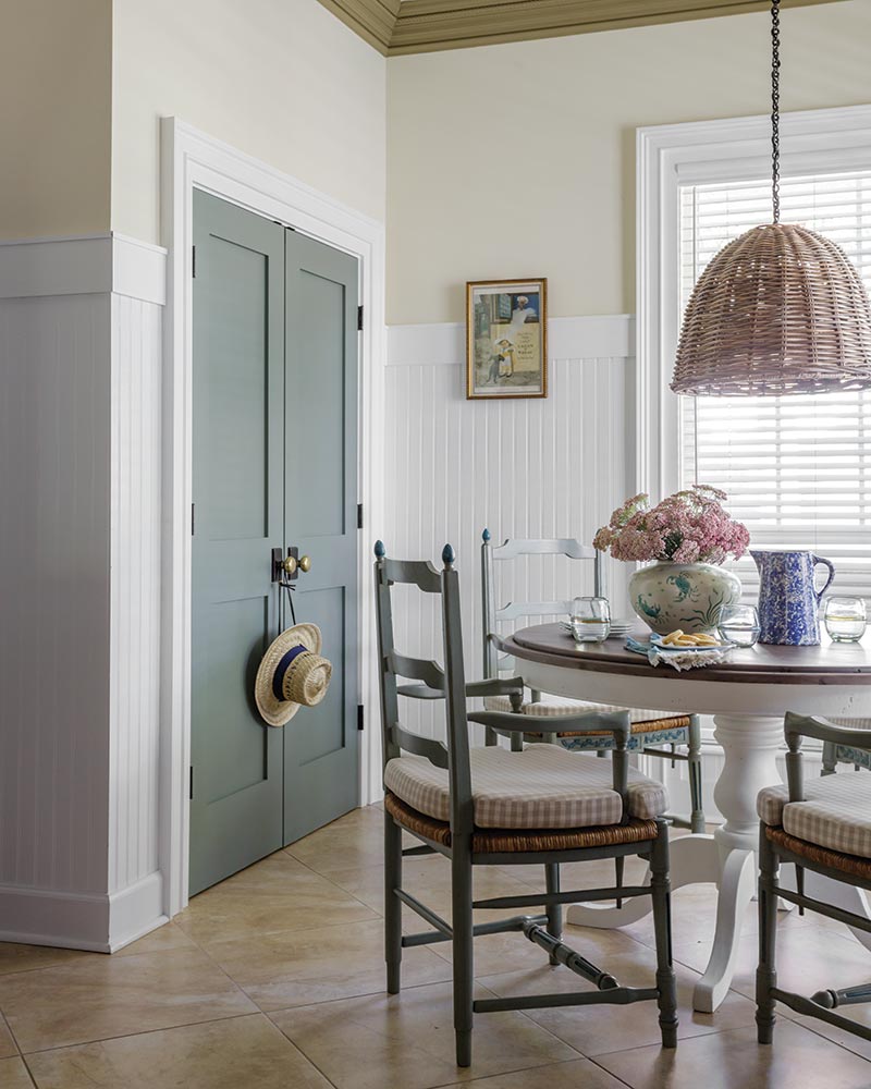 A dining nook with a round table, ladderback chairs, and a rattan pendant light.