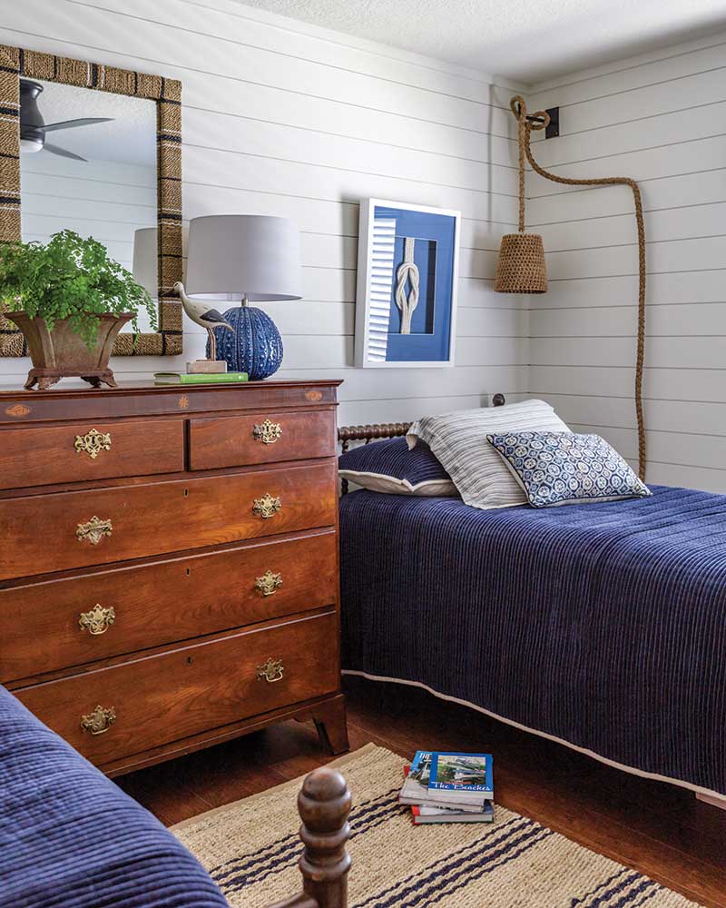 A bunkroom with white shiplap walls, blue bedding, and a framed nautical knot. 