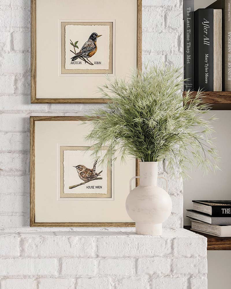 Two framed bird paintings on a white painted brick mantel. 