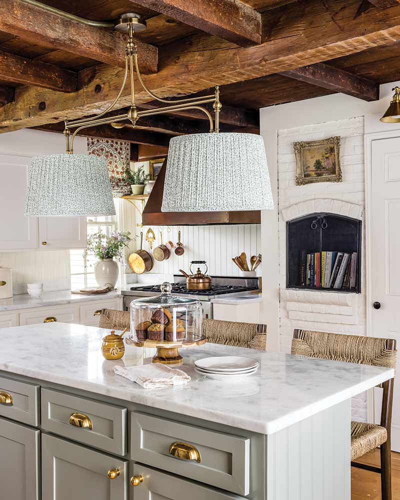 A kitchen with creamy cabinets, wooden beams, and marble counters.