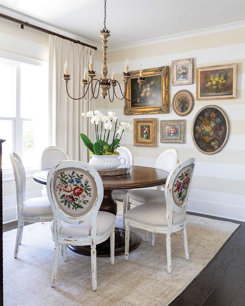 A dining room with embroidered chairs and a gallery wall of antique paintings. 