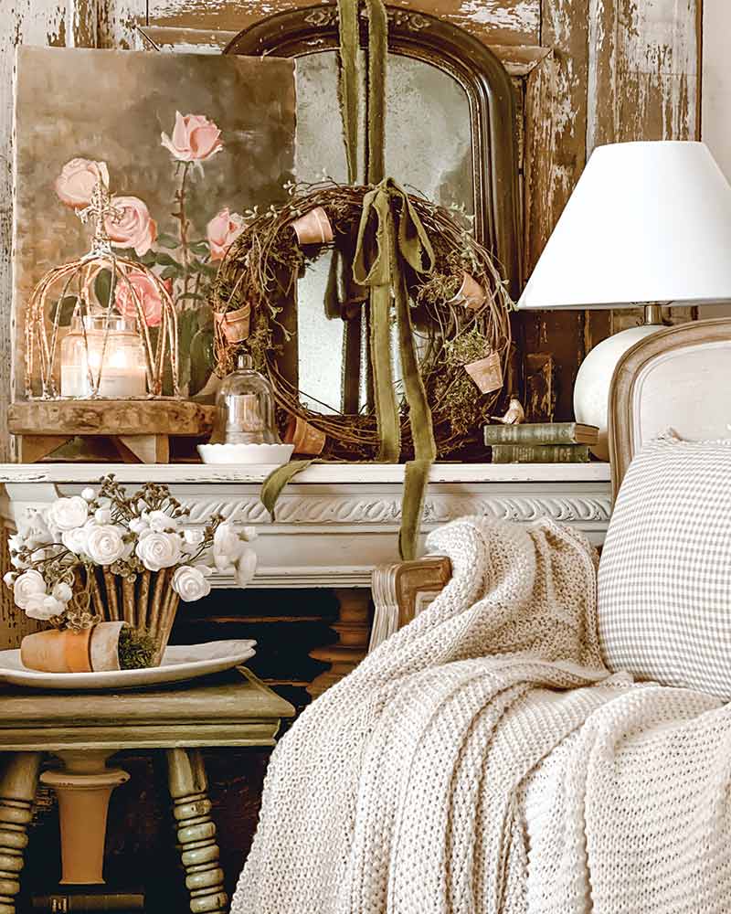 A living room with layered antiques on the wall and a French-style chair with a white blanket draping over the side. 