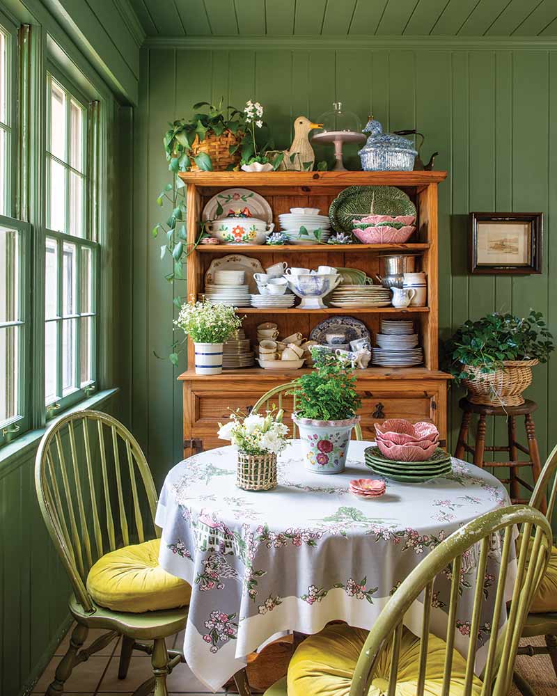 A breakfast room with a colorful wall painted green and a pine hutch filled with collected dishware.