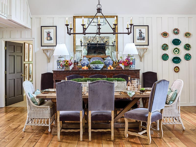 A traditional dining room featuring a long wooden table with six chairs, two of which are wicker armchairs at each end.The room is decorated with wall-mounted green plates and has white paneling.