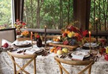 Our Top Picks for Thanksgiving & Holiday Hosting Essentials A Thanksgiving-themed dining setup with a table adorned with floral centerpieces, candles, and a fall-inspired decor, set against a backdrop of large windows overlooking green foliage.