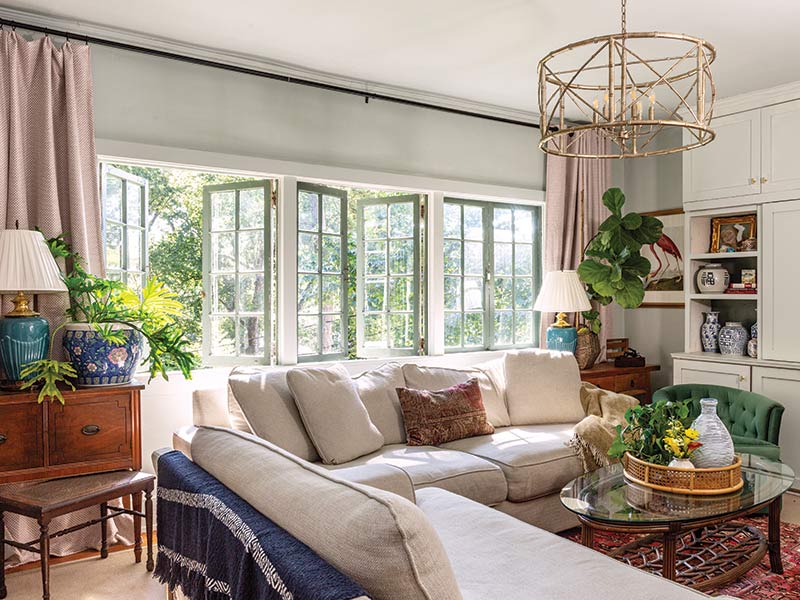 A living room with a wall of windows overlooking the trees. A large white sectional takes up most of the room.