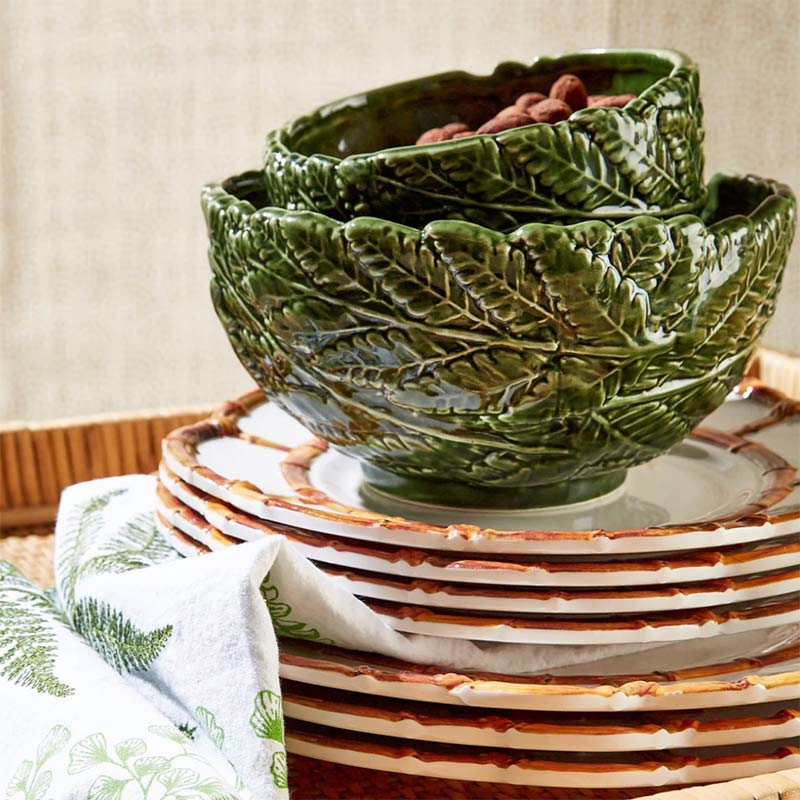 Green fern leaf bowls on a stack of white china with a bamboo border.
