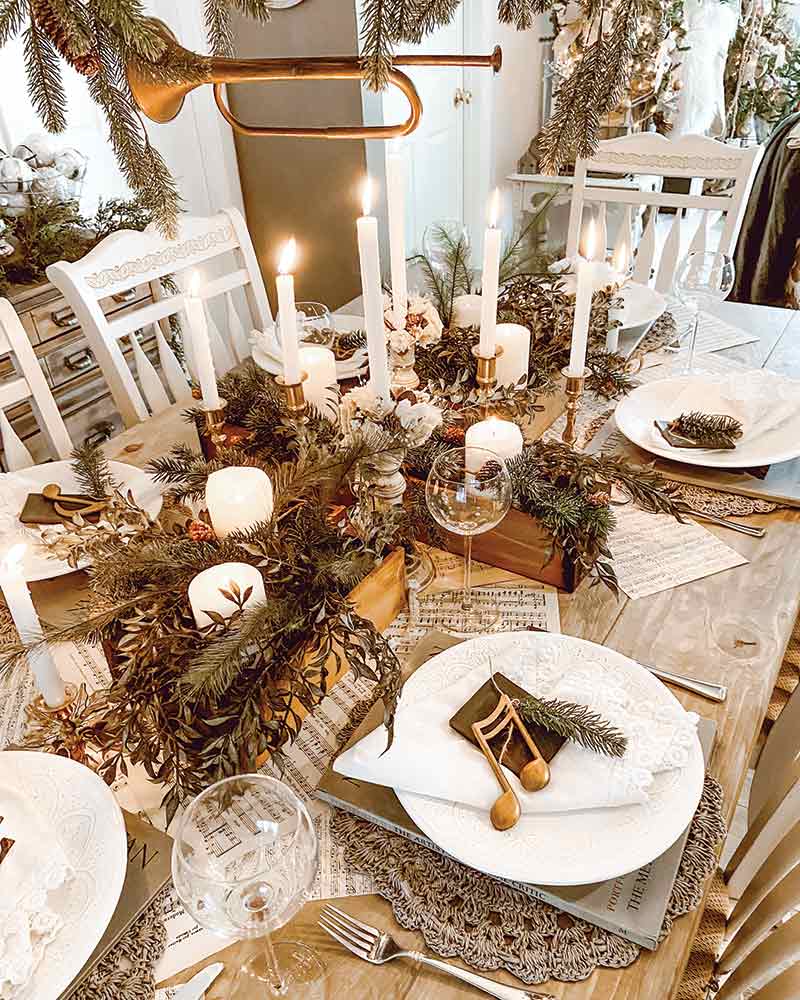 A rustic holiday tablescape with greenery, white dishware, and a musical note at each place setting. 