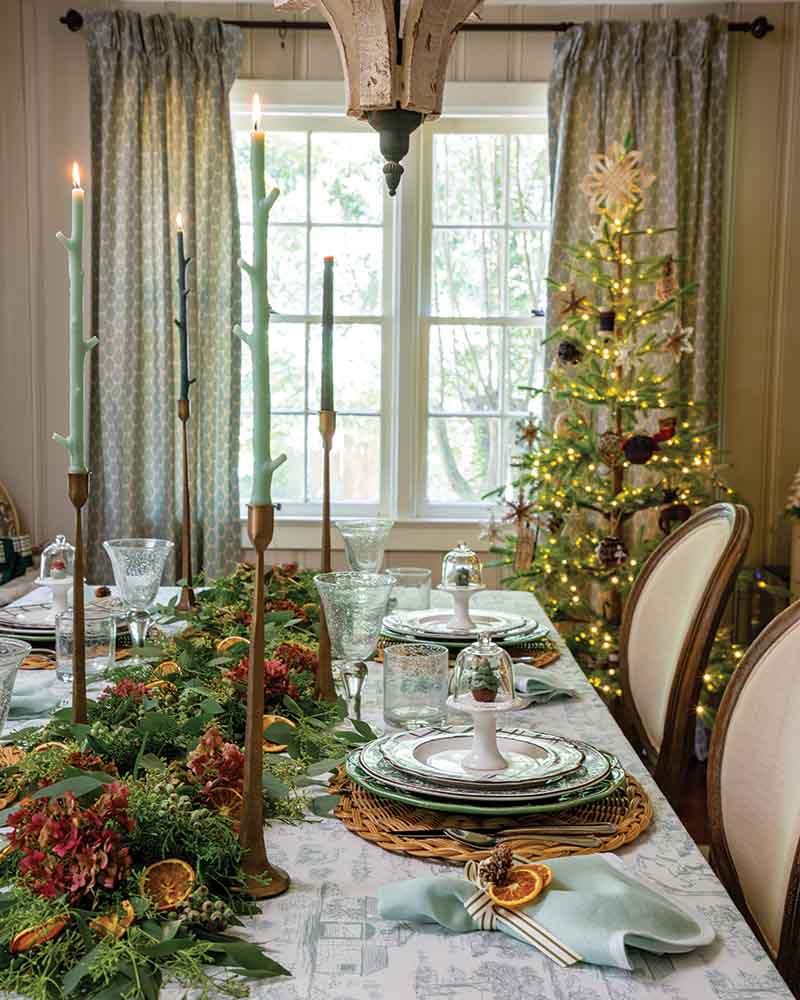 From foraged elements and woodland-inspired tapers to a tree bedecked in simple, rustic decorations, the forest-themed spirit of the room juxtaposes against sleek candlesticks and Louis XVI-style chairs. T