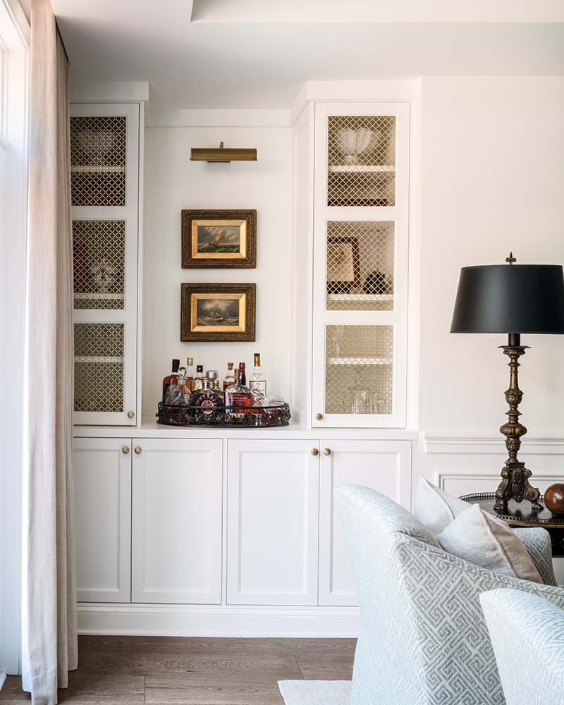 White paint, metal mesh inserts, and a library sconce elevate custom built-ins that serve as a living room bar.