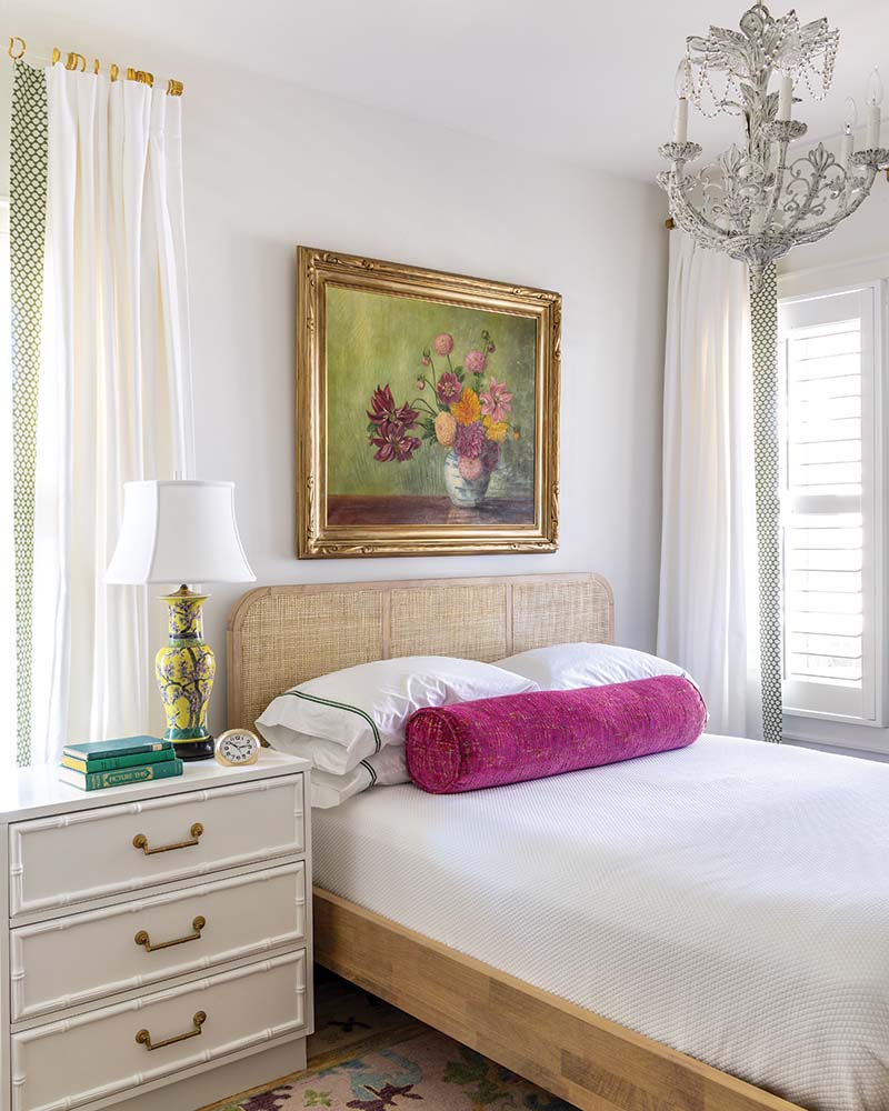 The guest bedroom takes a sharp turn from the homeowners’ more traditional space, showing off a vibrant charm in the form of a floral painting and a collection of vintage needlework.