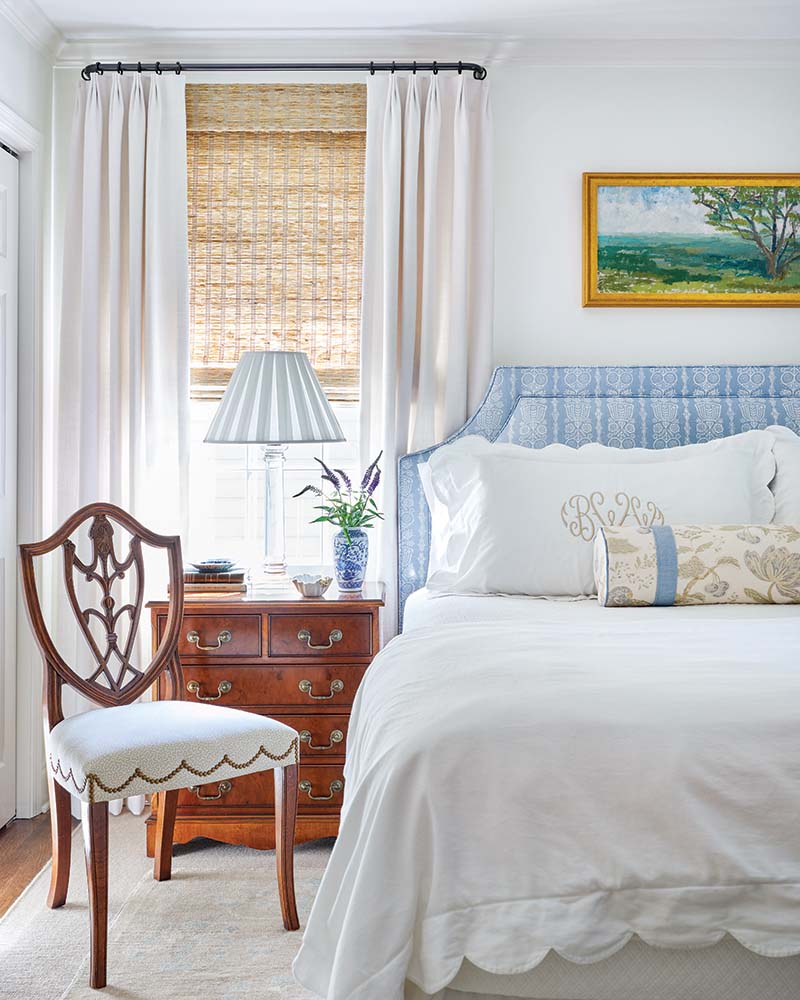 The primary bedroom takes a more formal approach as rich wood tones extend warmth to the tranquility of a blue-and-white palette. An upholstered headboard showcasing a print that serves as a play on stripes introduces a subtle contemporary element.