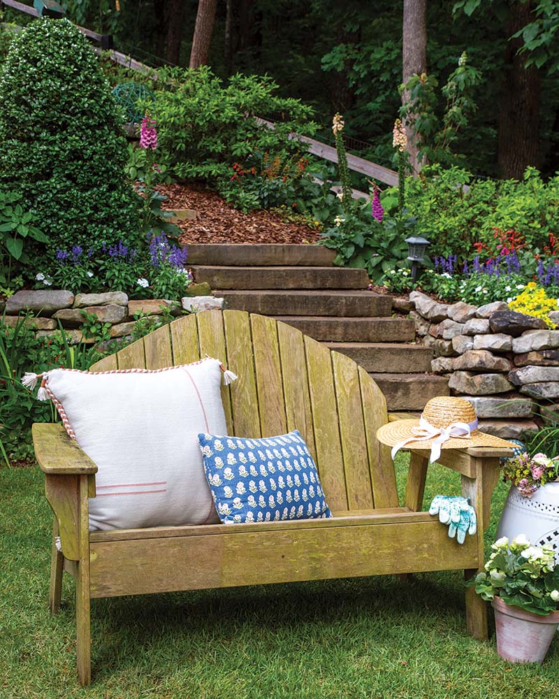 A wooden bench outfitted with plush pillows makes for the perfect perch to take in the garden’s glorious surroundings.