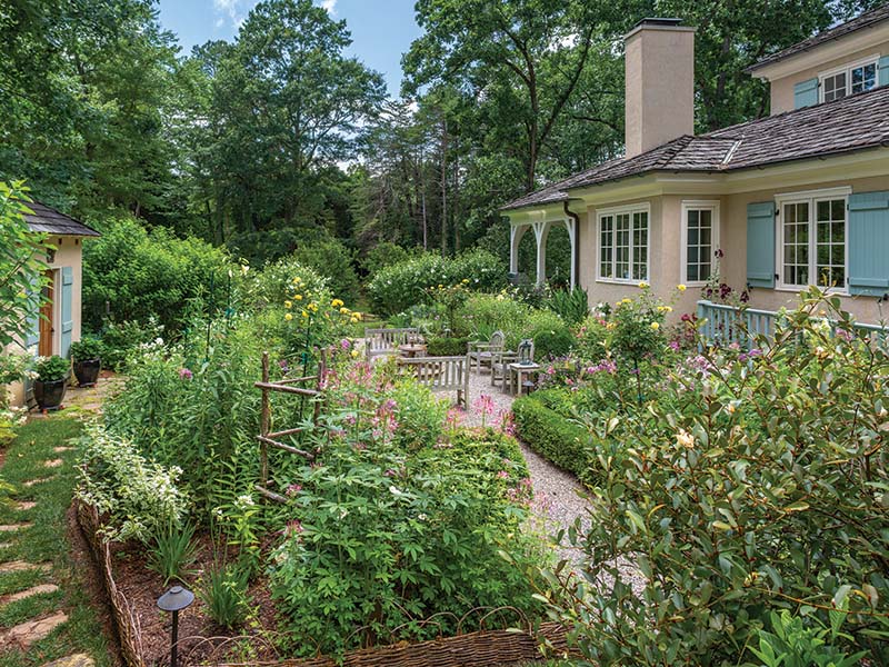 Stretching between the house and the potting shed, a lushly planted area provides a focal point from the kitchen, while an informal patio with Belgian block granite pavers and a parterre of English boxwoods serves as a gathering spot for family and friends.