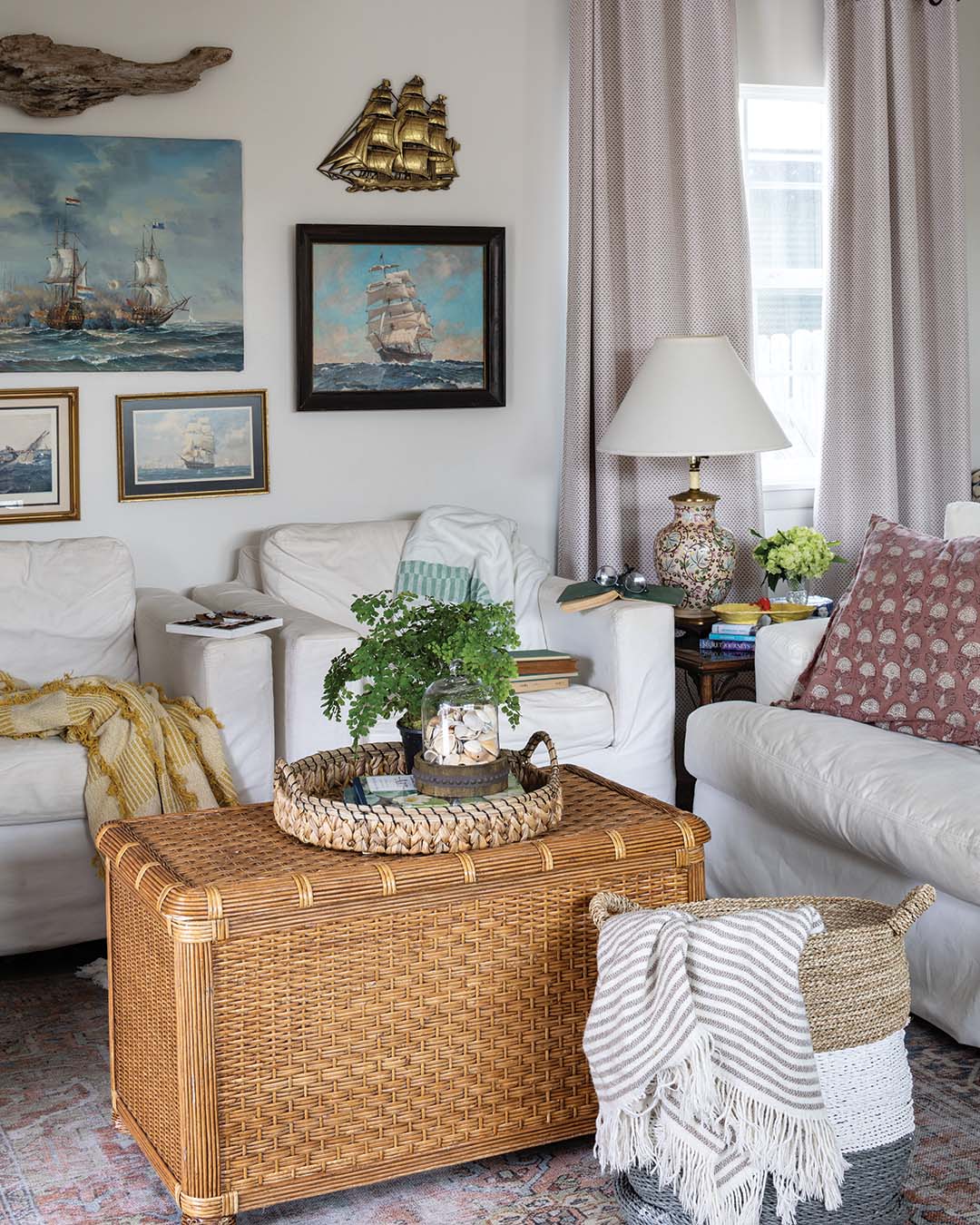 A comfortable white sofa coordinates with two armchairs, while an oversized woven basket doubles as storage and a coffee table. The gallery wall with paintings and prints collected from Florida to Chicago imparts a nautical touch.