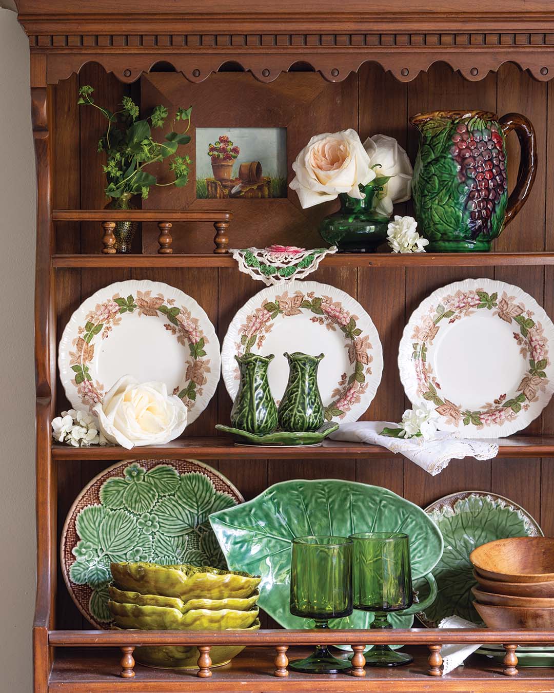 China decorated with a sweet floral motif livens the dining room, adding a touch of color against the wooden backdrop. Garden-inspired majolica catches the eye, lending a sense of whimsical personality as it echoes the natural scenery found just beyond the doorstep. A classic touch, white roses balance the display and bring a sense of grounded simplicity to the colorful exhibit.