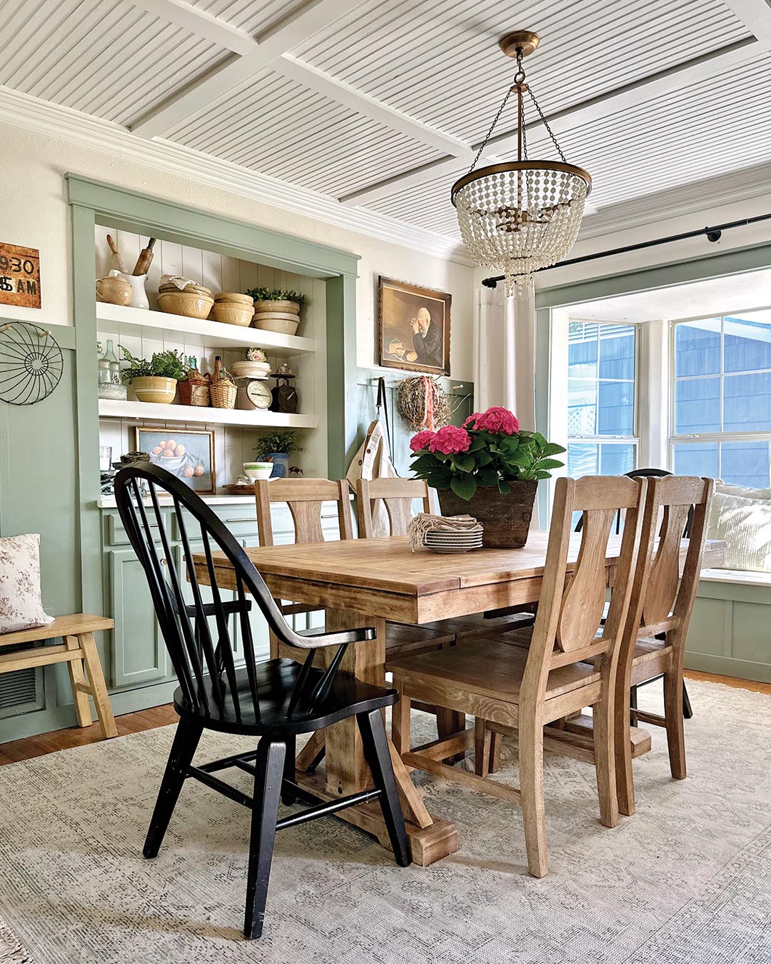 The kitchen opens to the dining room, where wainscoting and built-ins painted Card Room Green by Farrow & Ball, the same shade used for the kitchen island, create a cohesive feel between the two spaces.