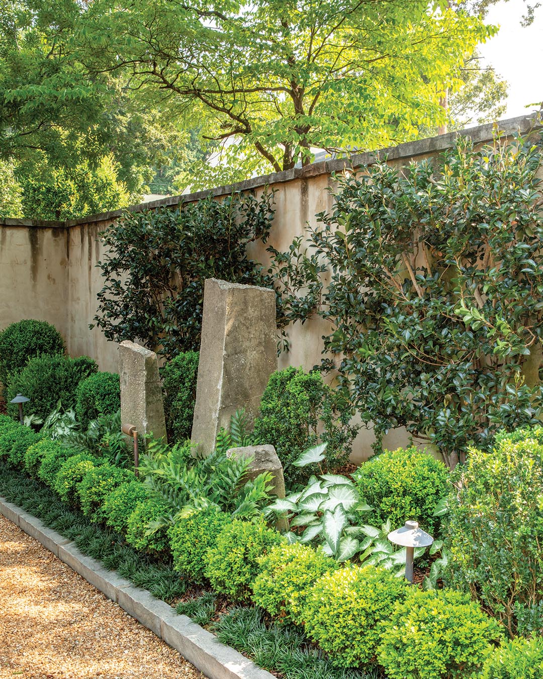 From day one, the trio envisioned how the wall framing the garden would look, knowing it needed to complement the intricate stone structure of the home. Daniel, branch manager at Father Nature Landscapes, explains how the hand-chiseled limestone is stacked in an ashlar pattern, an incredibly time-consuming yet artistic form of masonry. “Having this fabulous stone, a handsome porch, and nice details like terra-cotta chimney pots [creates] an easy backdrop to work with,” Daniel says.