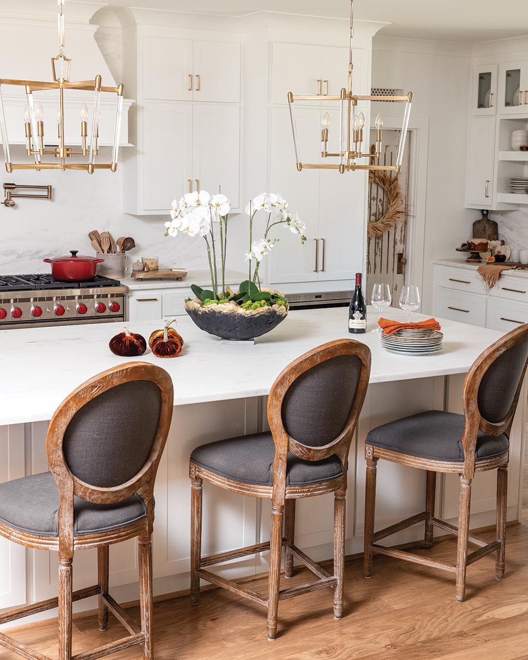 A duo of caged pendant lights infuses the traditional design with a dash of modern influence as it ties in the cabinetry’s gold hardware.