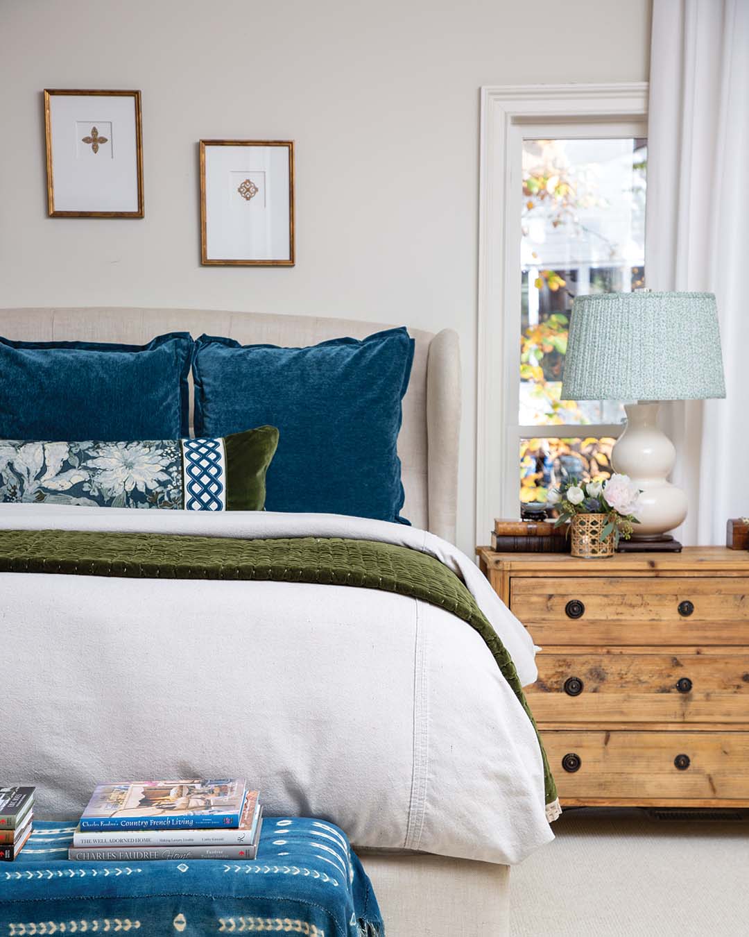 Emerald green accompanies indigo in the primary bedroom, with the featured fabric of the coordinating bolster and throw pillows serving as the setting’s muse. Lighter wood tones and crisp white bedding contribute to the light and airy aesthetic.