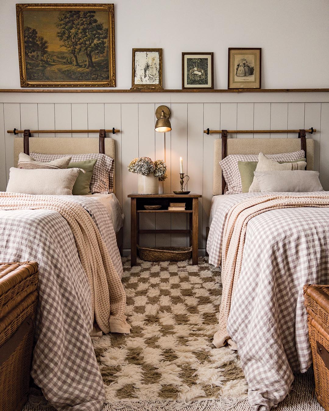 The guest bedroom, which features two twin beds, embraces a hint of pattern with a brown-and-white gingham echoed in both the rug and bedding. Vintage prints adorn the wall above the hanging headboards while a brass sconce serves as a reading light.