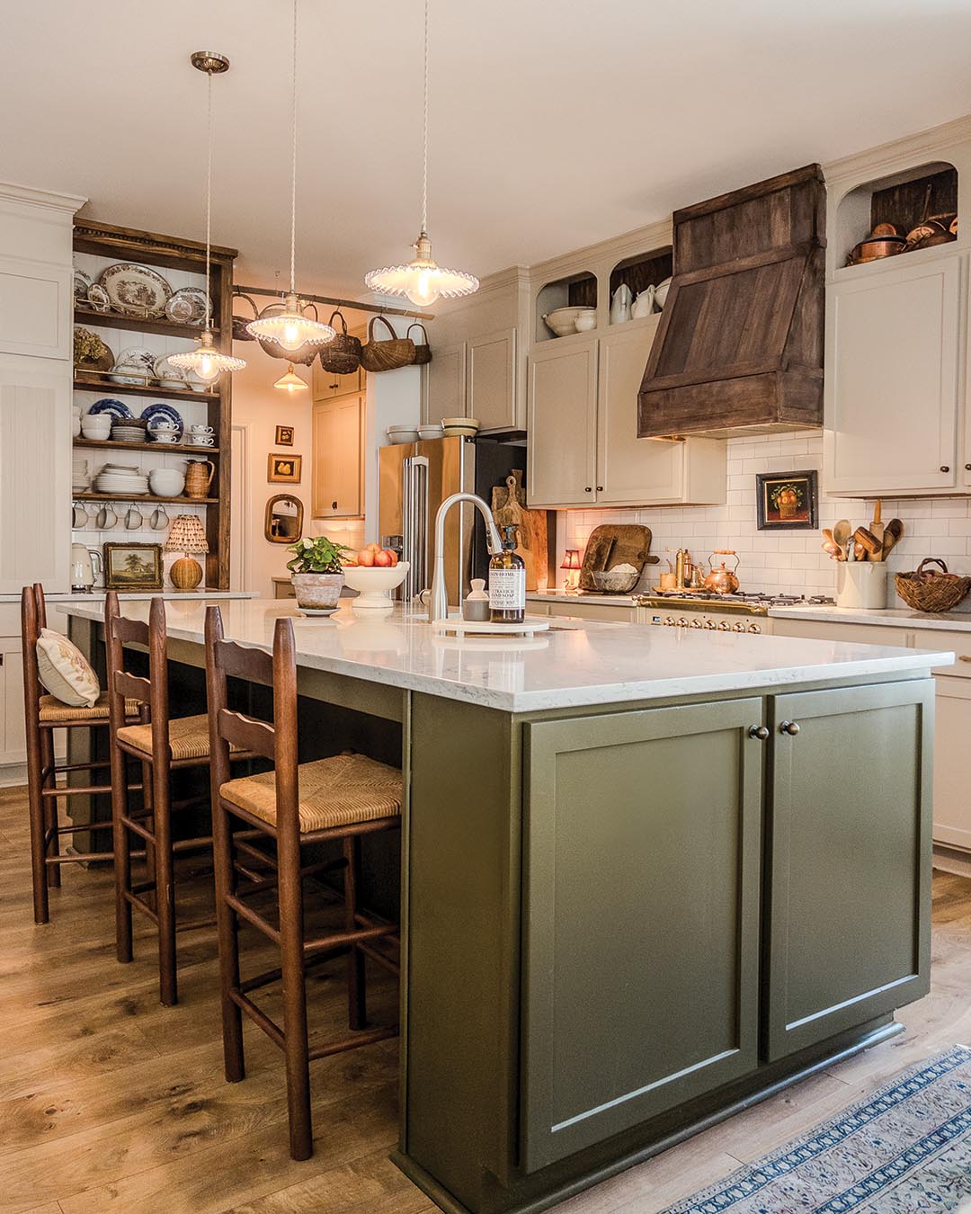 In the kitchen, the wood range hood and coordinating shelf showcase Emi’s appreciation for nature-inspired design—especially with the earthy green tone of the island, painted Cardamom by Farrow & Ball. The surrounding cabinets coated in Farrow & Ball’s Roasted Macadamia create a creamy backdrop emphasized by the white quartz counters. Emi extended the cabinets to the ceiling, which allowed for a few small alcoves that display her ironstone and copper pieces.