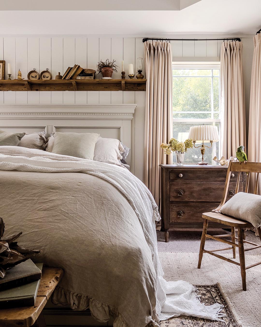Layering is key when it comes to infusing a neutral space with warmth and coziness. Small collectibles—from miniature artwork to timeworn tomes—stand out against the crisp white of the vertical paneling.