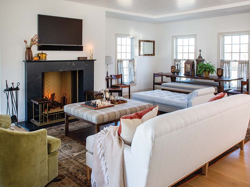 Adjacent to the kitchen, the sitting room can lean warm or airy, depending on the weather outdoors. Nicole and her team “scoured the globe” for a fireplace fender that would suit the space and had the rest of the fireplace built around it. The snug green accent chairs were chosen for their swivel, and other low-back pieces made the space more practical for multiple people to share.