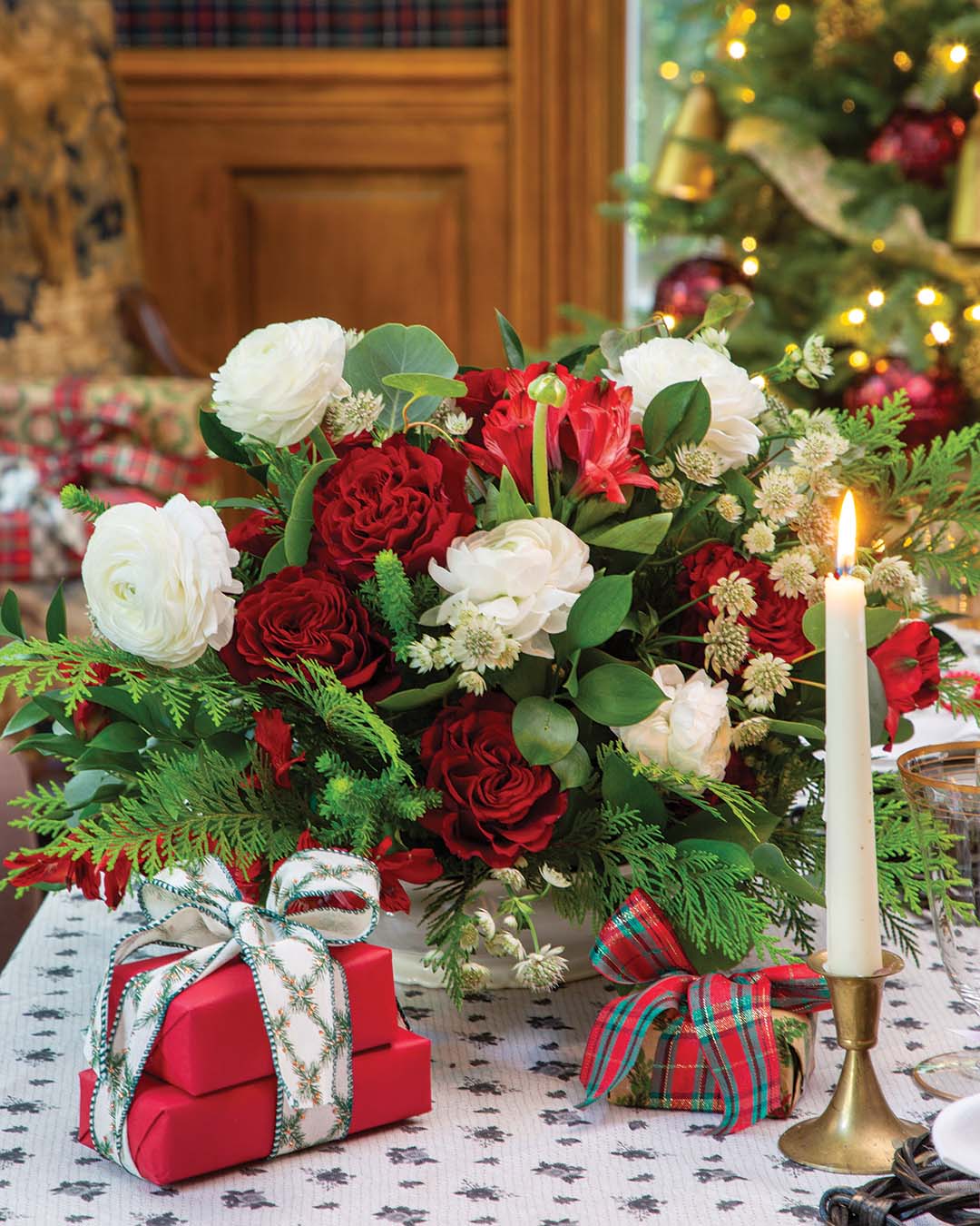 At the heart of the table is a bouquet of fresh scarlet and cream roses, sprinkled with sprigs of lush greenery to add a natural flair to the setting.