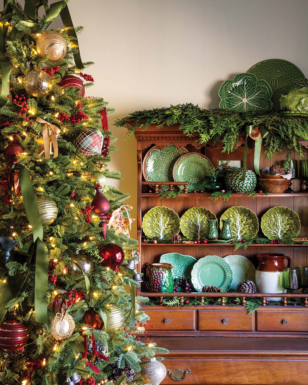 A classic Christmas tree glimmers with a mix of traditional baubles and glittering ornaments, complete with satin curls of moss green ribbon for added elegance. Red berries and pine cones tucked between each branch bring a subtle flourish of rustic flair.