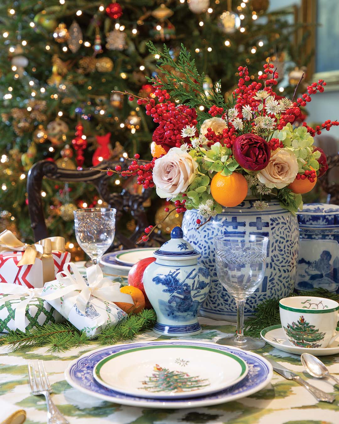 A stunning floral centerpiece atop a green ikat-patterned tablecloth catches the eye. Soft cream roses provide a sense of sophistication, while burgundy blooms add deep, radiant color to the display. Bright red winter berries offer a festive note, accented by sprigs of greenery that impart fresh contrast to the bouquet.
