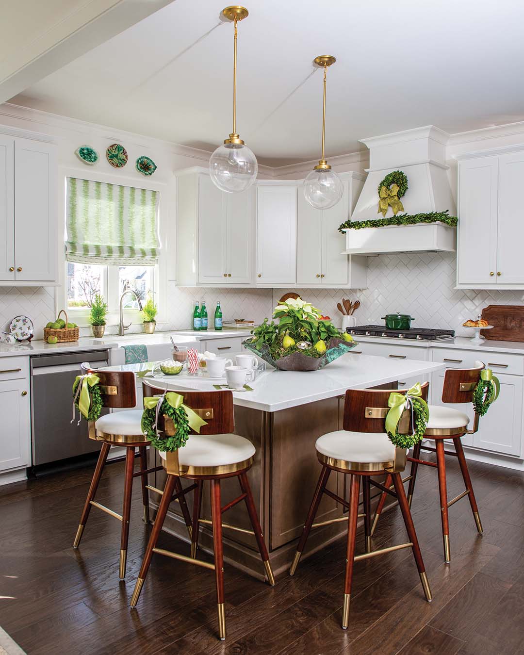 The predominately white kitchen features pieces from Kate’s majolica collection that hang artfully over the sink as well as tailored boxwood wreaths that dress up the barstools for the holidays along with fresh pears and poinsettias, all in the signature hue.