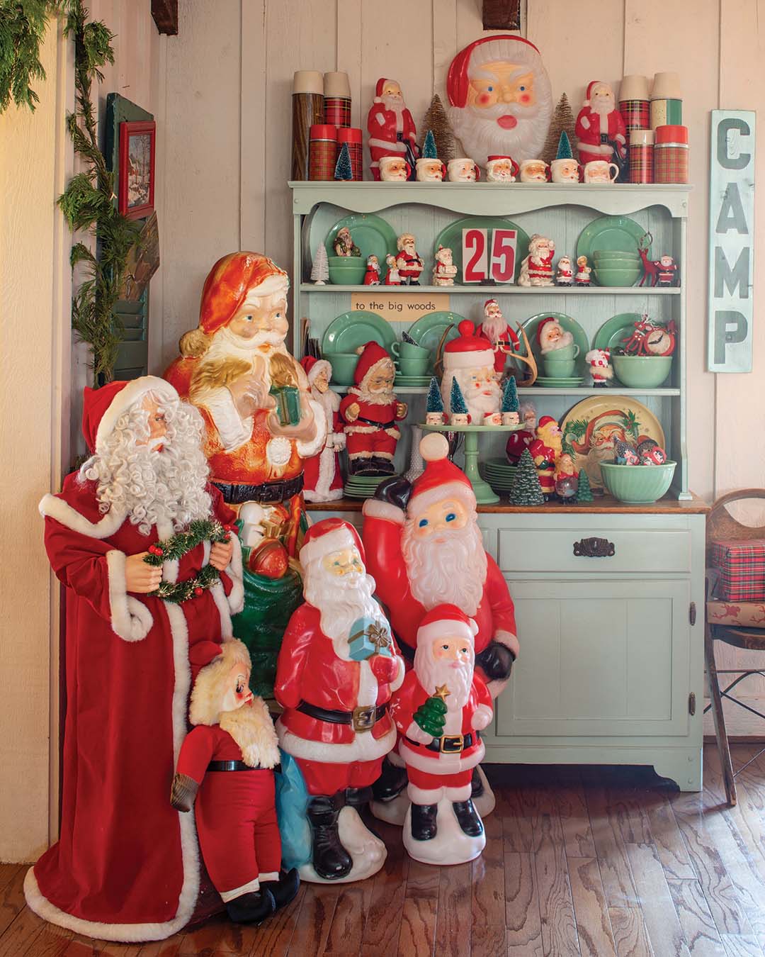 An assemblage of Santas in various sizes brightens the space nearby. The smaller figurines and mugs mingle with jadeite dishware, bottle brush trees, and vintage plaid thermoses, lending a sprightly spectacle to the shelves of the mint green hutch.