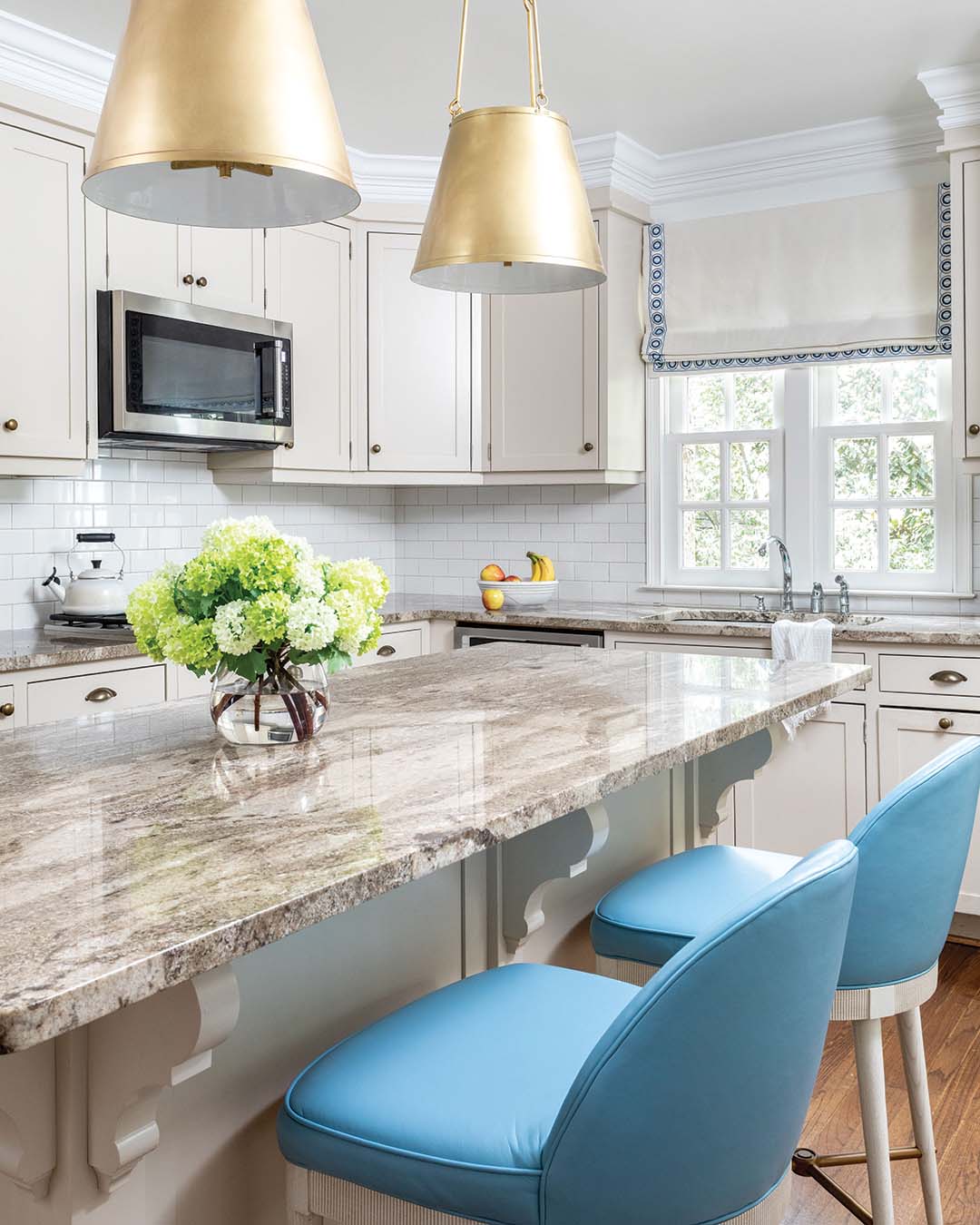 Updates to the kitchen remained largely cosmetic, as the existing finishes lent themselves well to a refresh. New light fixtures, vibrant barstools, and a bordered roman shade above the sink injected the space with personality while incorporating the homeowner’s beloved blue shades.